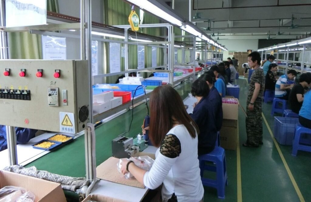 Workers sitting on blue stools assembling products in a brightly lit factory with conveyor belts and boxes, illustrating product assembly services China offers for efficient manufacturing